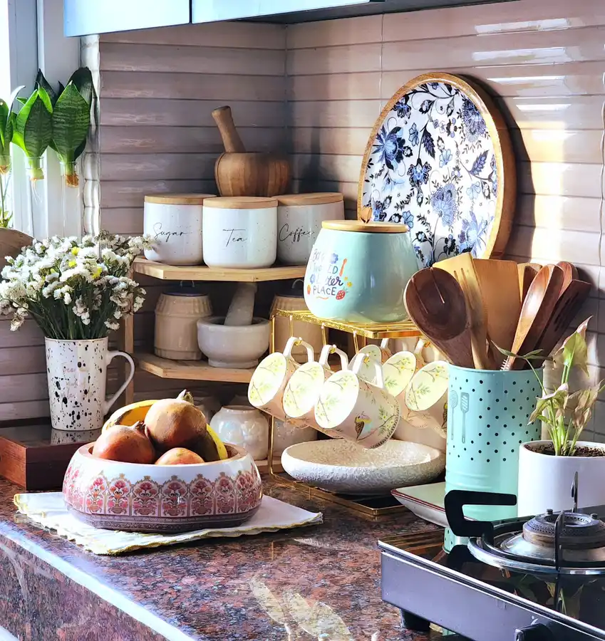 Colorful kitchen counter with patterned mugs, ceramic canisters, wooden utensils, fruit bowl and flowers