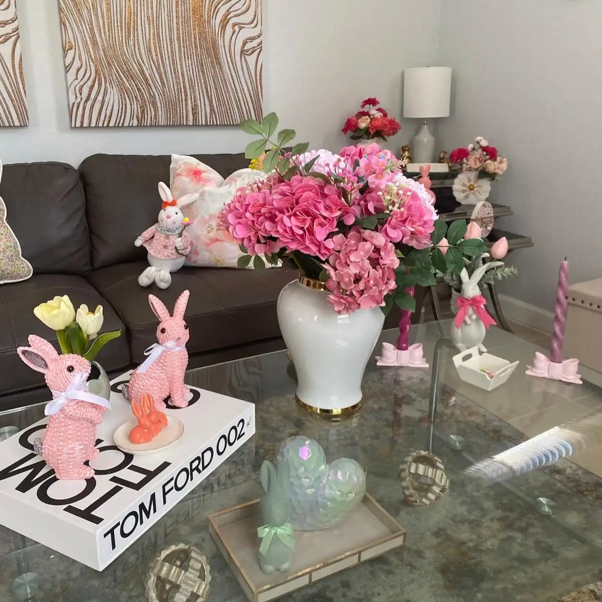 Playful Easter coffee table decor with pink flowers, bunny figures, pastel candles, and stacked books