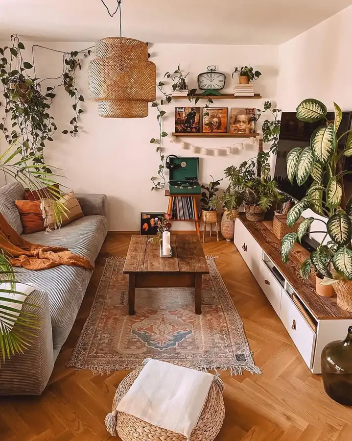Plant-filled living room with a record player, vinyl albums, trailing greenery, woven baskets, rough wood table, and TV console.