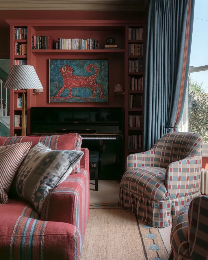 Colorful living room with rust built-in shelves, striped sofa, blue plaid chair, blue curtains, patterned cushions, and artwork