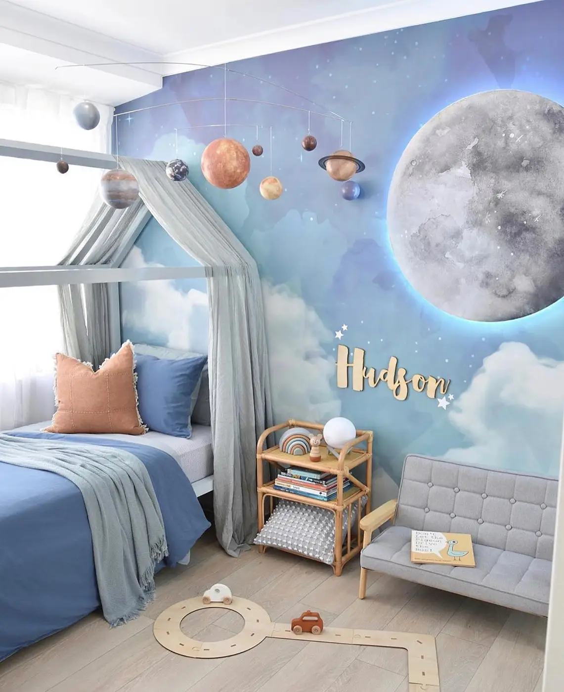 Soft blue bedroom with hanging planets above the bed, pale canopy, and moon mural background