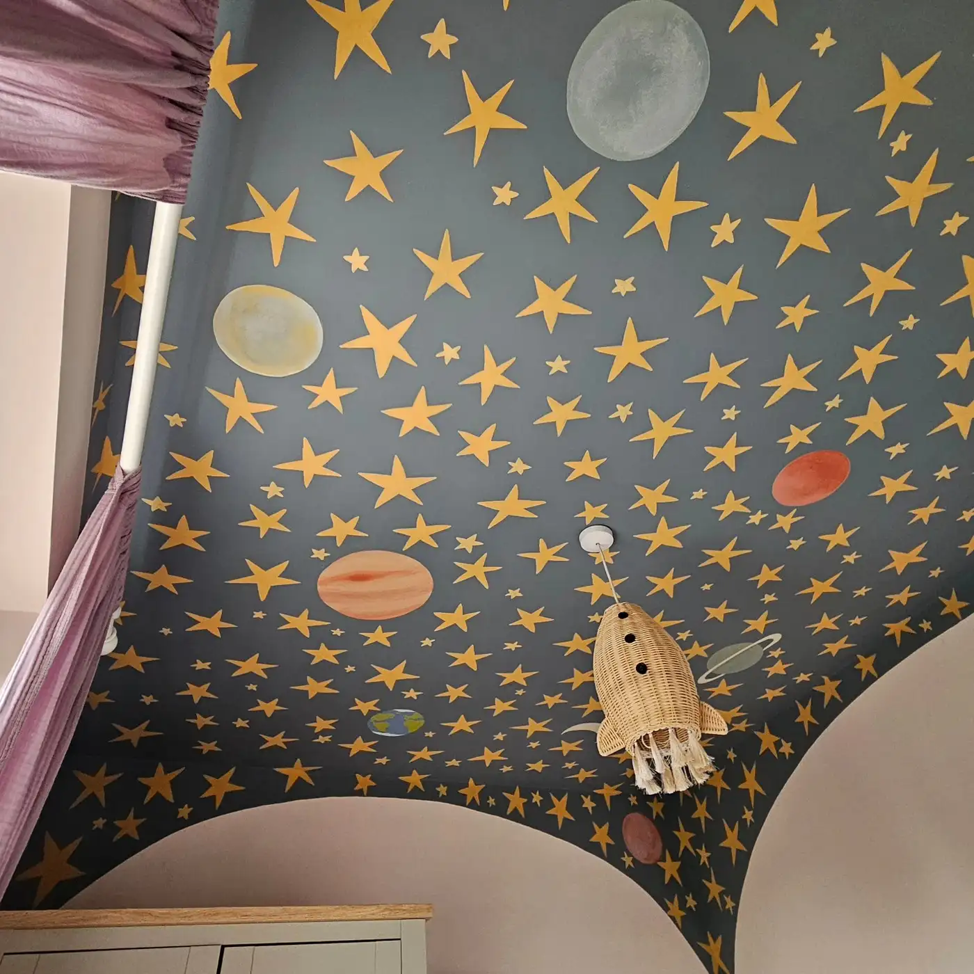 Bedroom with sloped dark ceiling covered in stars, planets, moons, and rocket illustrations