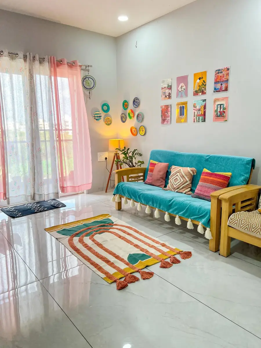 Cheerful living room with a turquoise sofa cover, coral cushions, pink curtains, colorful rug, wall prints, and painted plates.
