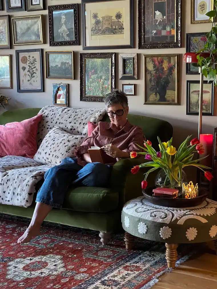 Eclectic living room with green sofa, dense gallery wall, patterned rug, round ottoman, tulips, and floor lamp