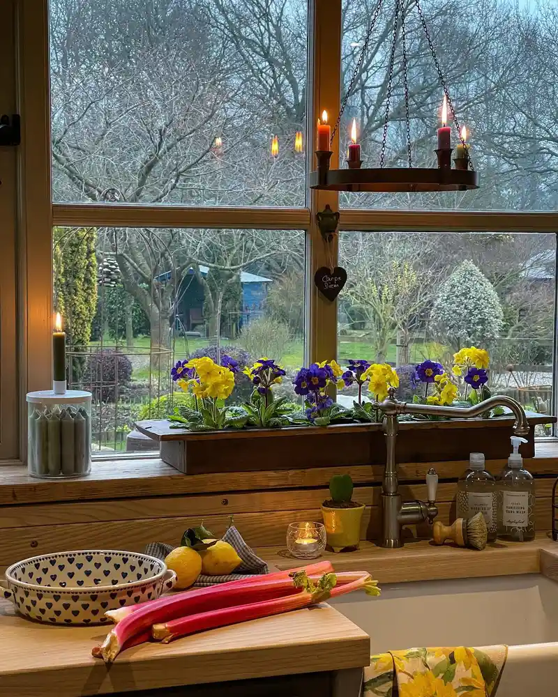 Kitchen window sill with long wooden planter filled with yellow and purple flowers