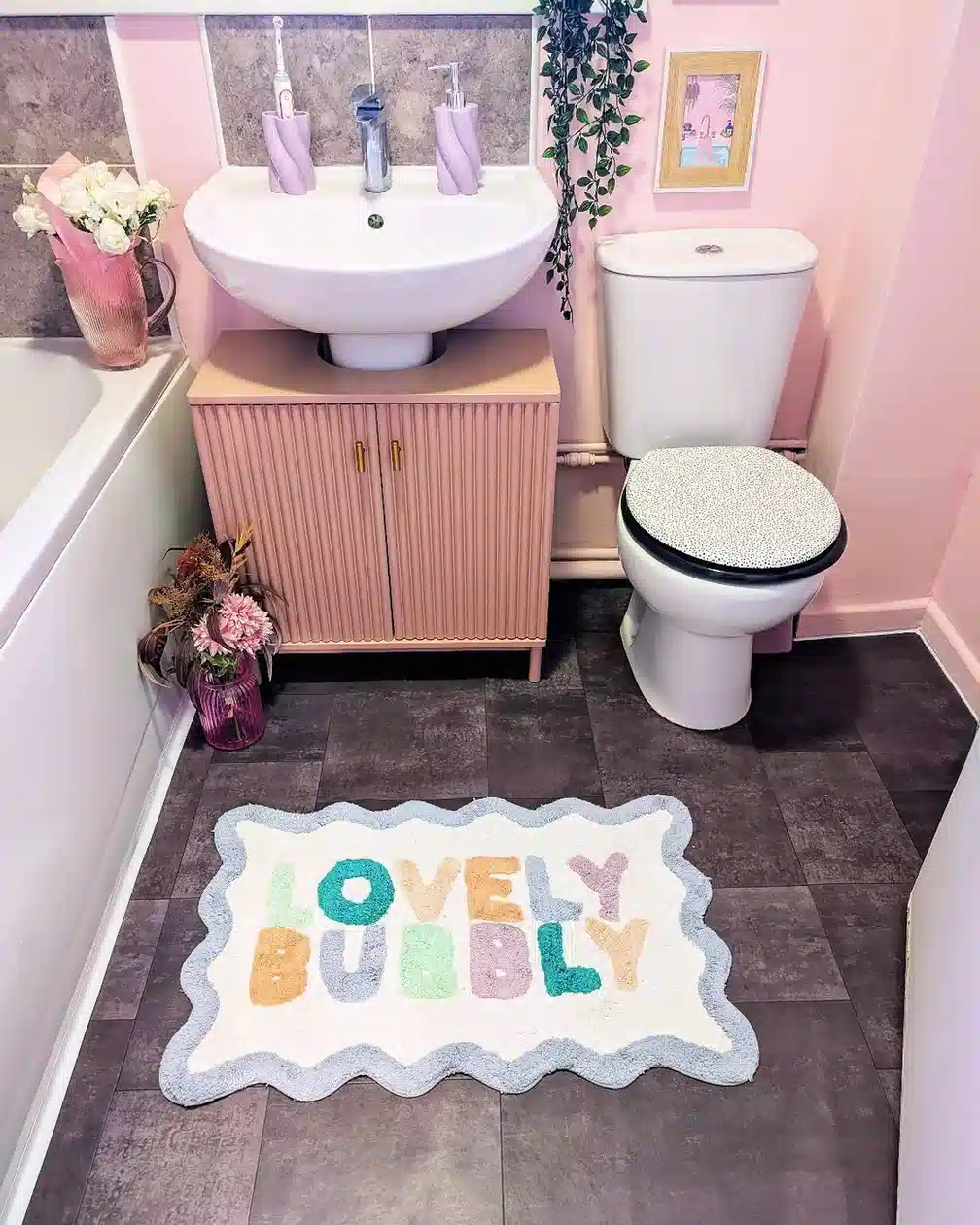 Soft pink bathroom with fluted vanity, round mirror, and colorful wavy bath mat