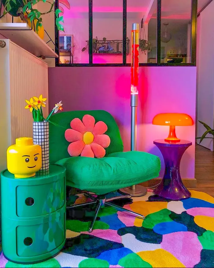 Bold colorful corner with bright green chair, purple side table, orange lamp, yellow decor, multicolor rug, and pink lighting