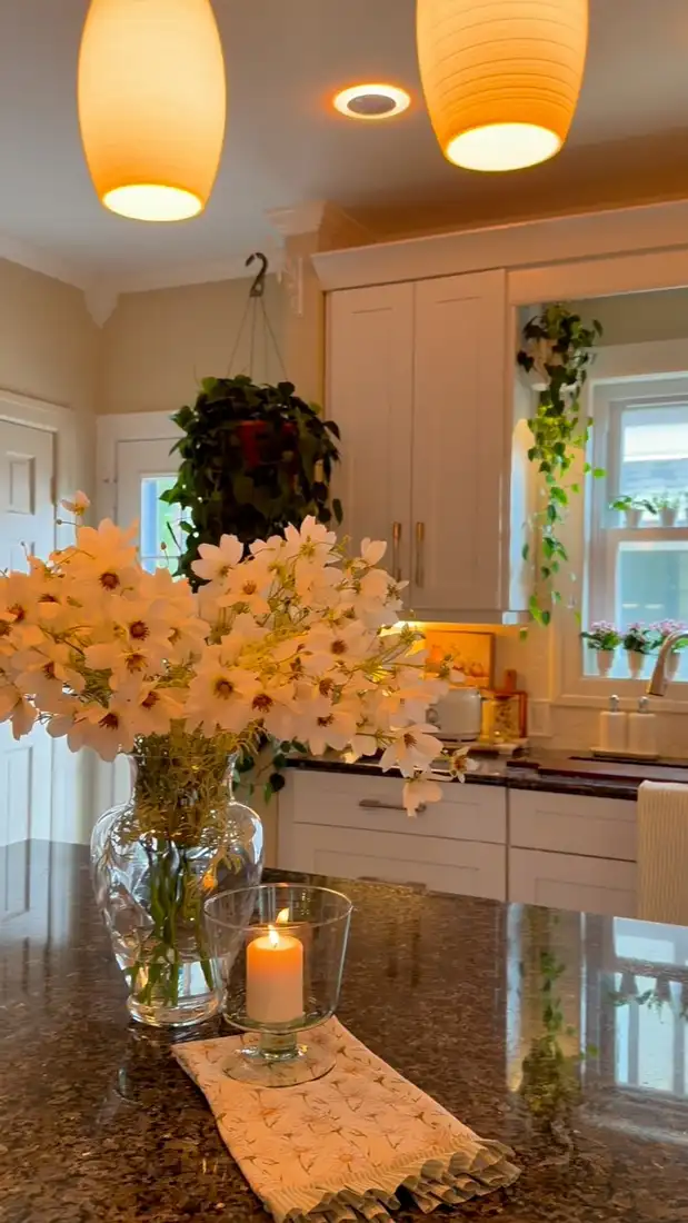 Kitchen window sill with several small pots of pink flowers and trailing greenery nearby
