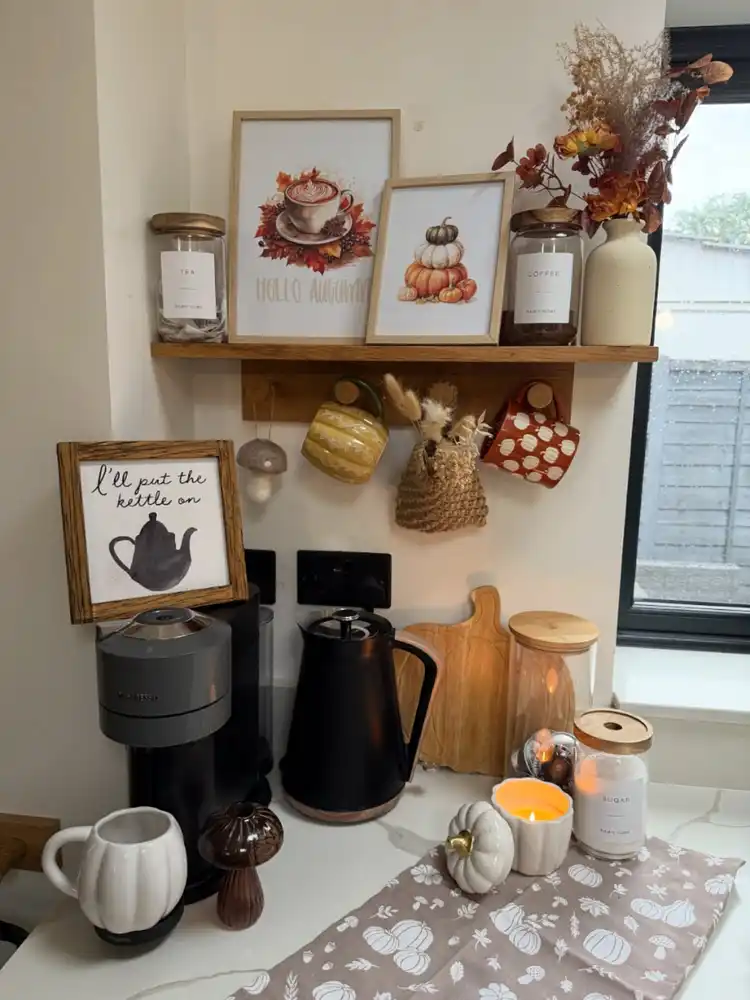 Simple fall coffee station with black appliances, mustard and rust mugs, small pumpkins, candle, and autumn wall art