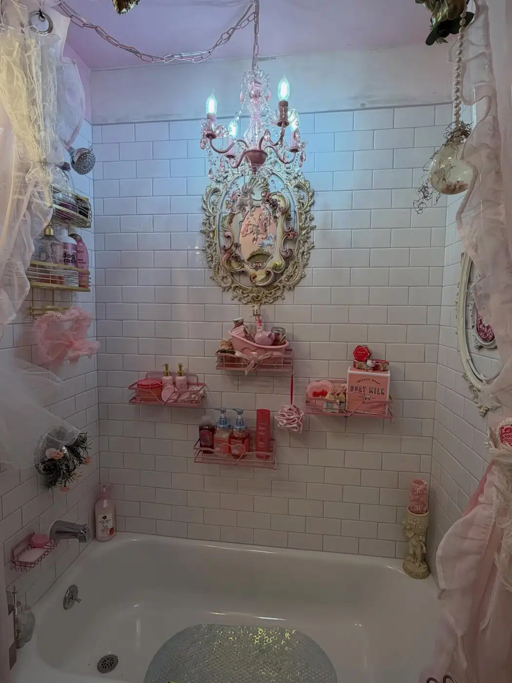 White bathroom with freestanding tub, crystal chandelier, ornate mirror, and pink accessories