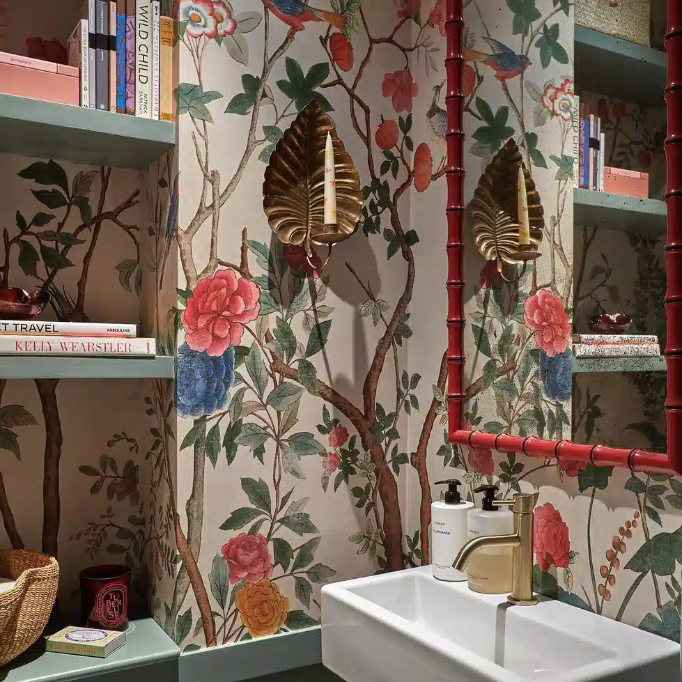 Bathroom with bold botanical wallpaper, red bamboo-style mirror, and simple white sink