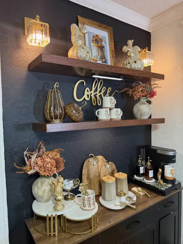 Moody fall coffee station with black wall, wooden shelves, metallic pumpkins, dried flowers, gold accents, and brown mugs