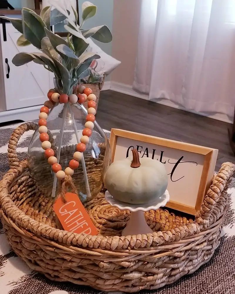 Fall coffee table tray with a pale green pumpkin, orange bead garland, clear vase with greenery, and woven textures