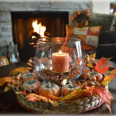 Round fall coffee table centerpiece with a glass candle holder surrounded by small pumpkins, berries, acorns, and autumn leaves