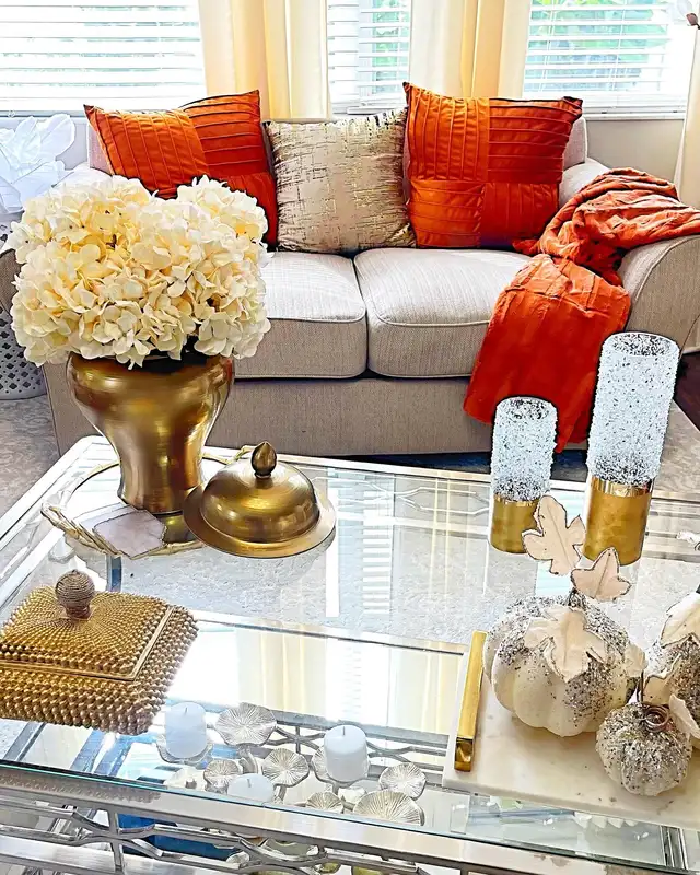 Glam fall coffee table decor with gold accents, pale pumpkins, candle holders, cream flowers, and sparkling decorative pieces