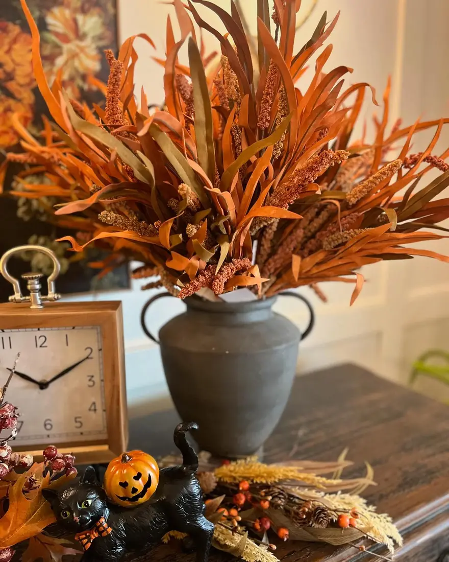 Dark matte vase filled with tall burnt orange fall foliage on a coffee table with small neutral decorative accents