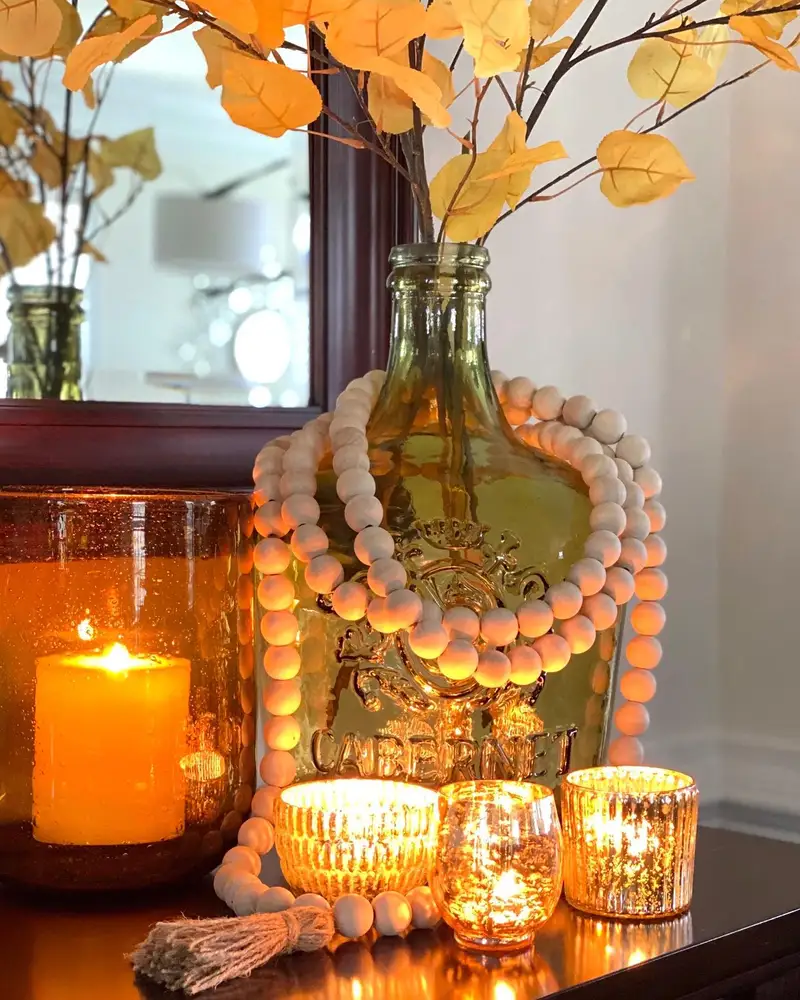 Cozy fall coffee table with amber glass bottle, autumn branches, wooden bead garland, and glowing candles