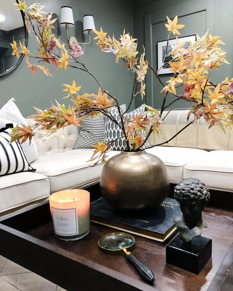 Large bronze vase with loose orange and gold maple branches styled with dark books and sculptural accents on a coffee table