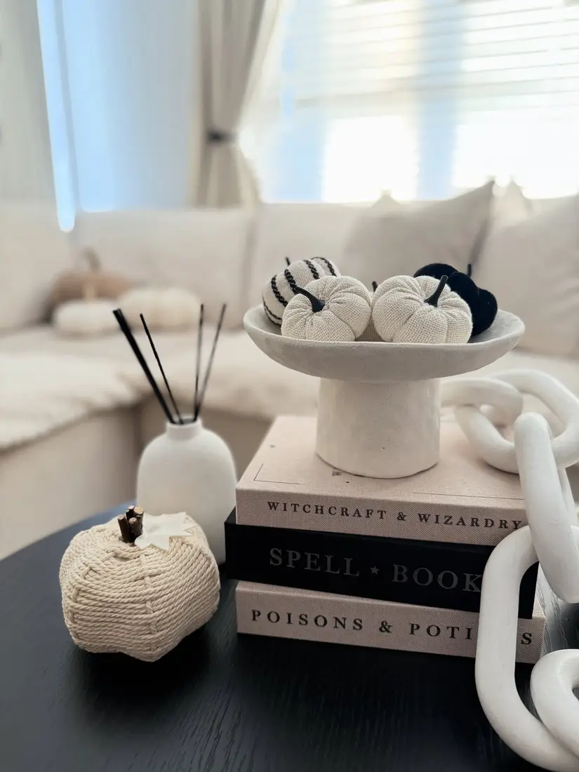Black and cream fall coffee table with knitted pumpkins in a raised bowl, stacked books, white chain decor, and neutral accessories