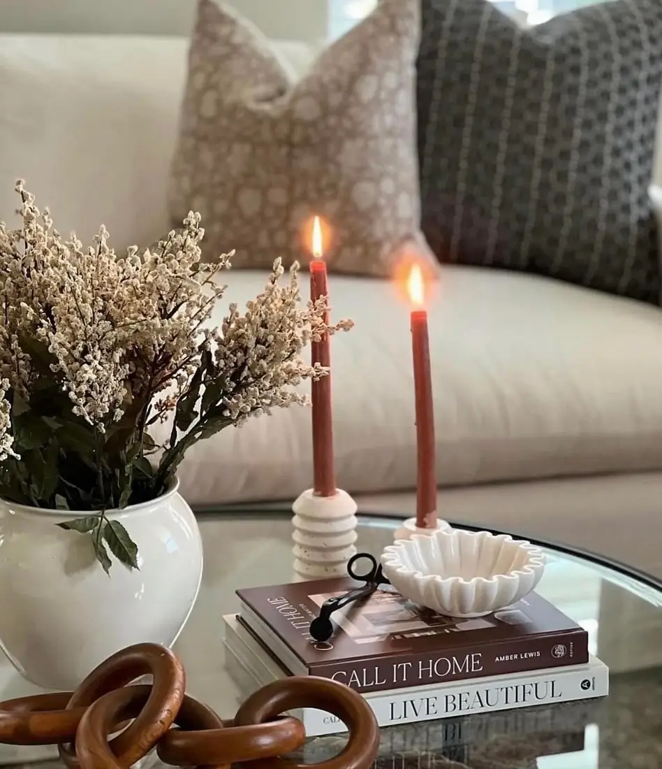 Neutral fall coffee table with rust colored taper candles, white flowers, stacked books, white pottery, and chunky wooden chain decor