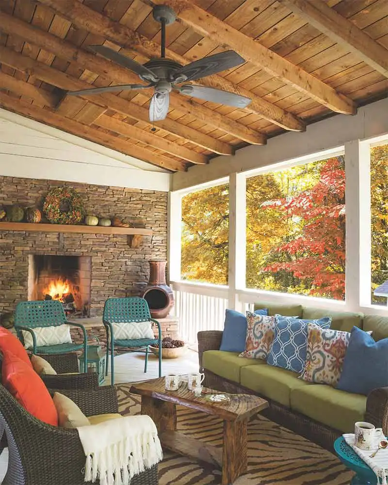 Covered porch with wood ceiling, stone fireplace, wicker seating, blue cushions, and woven rug