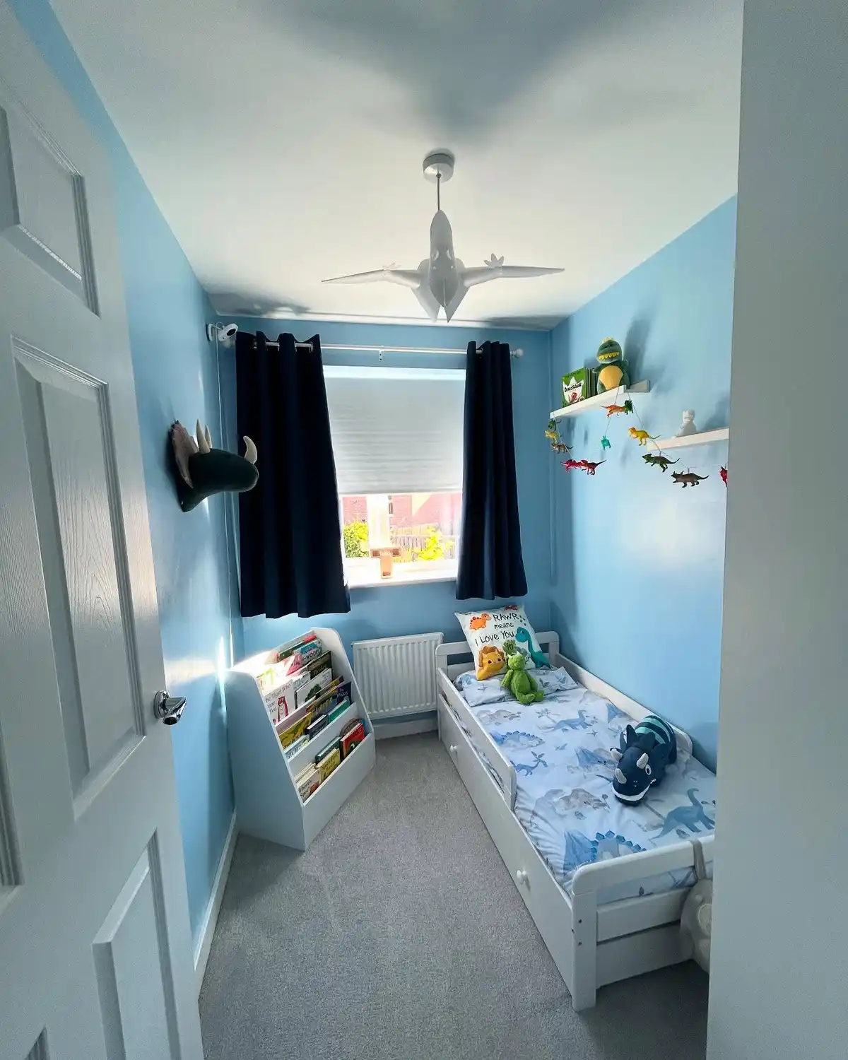 Narrow kids bedroom with single bed under the window, wall shelves, and slim book storage