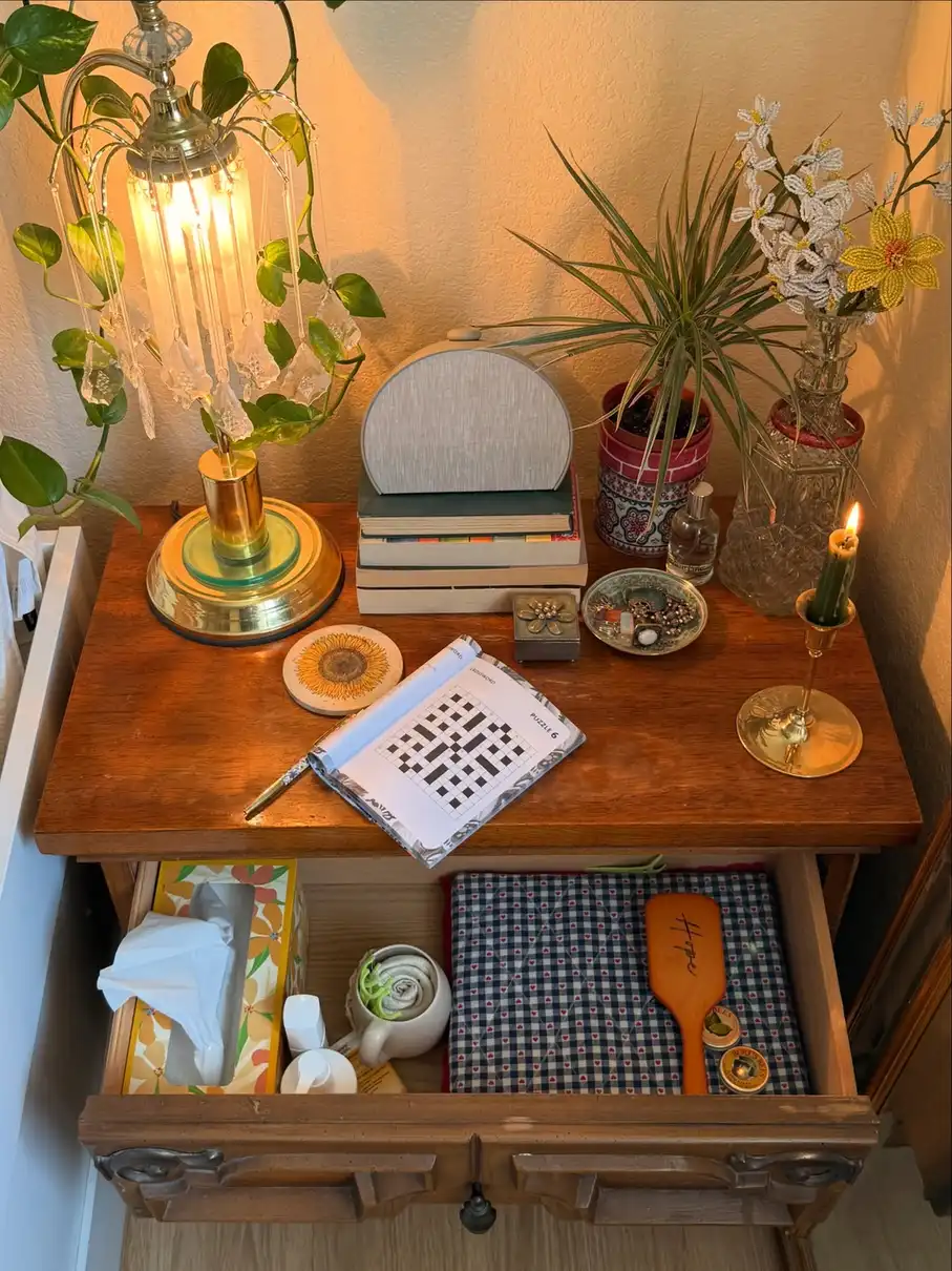 Wood nightstand styled with glass lamp, books, green plants, candle, and everyday bedside items