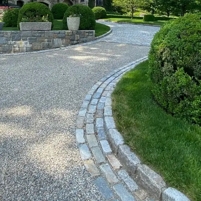 Gravel driveway with a curved stone border separating the gravel from a dense green hedge