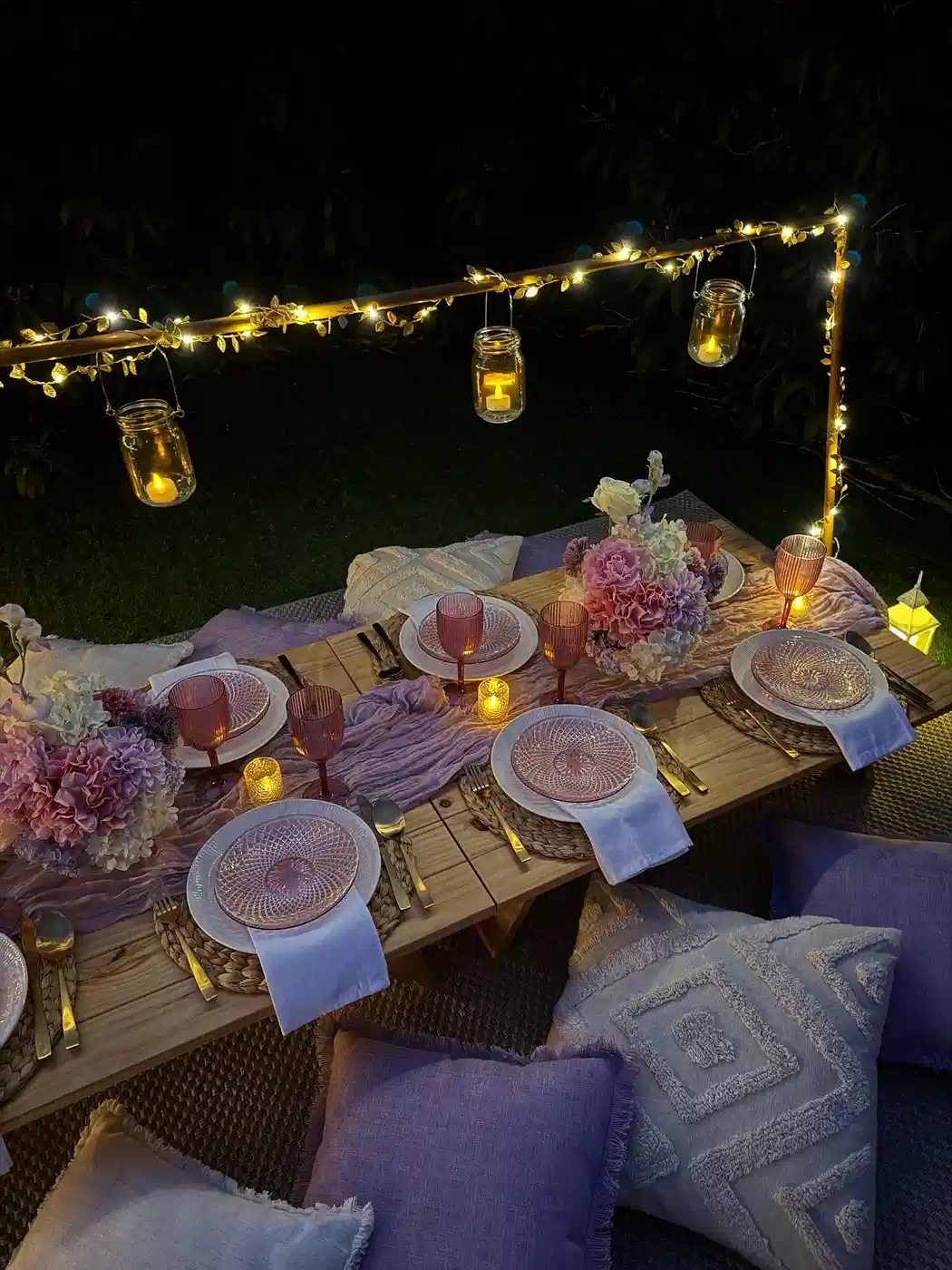 Outdoor dinner table illuminated by warm string lights with elegant place settings and candles