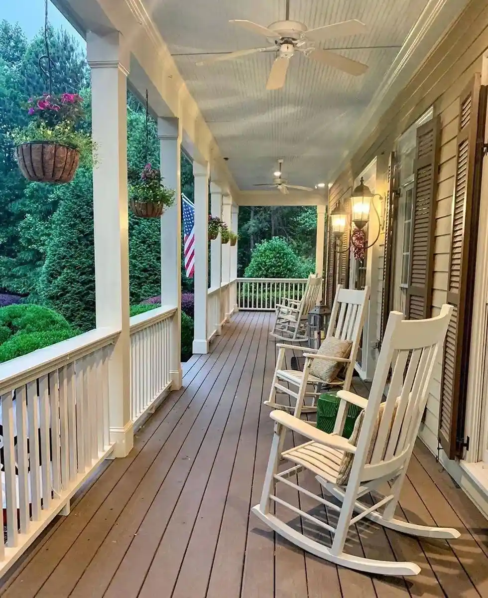 Long covered porch with white rocking chairs, hanging baskets, white railing, and ceiling fans