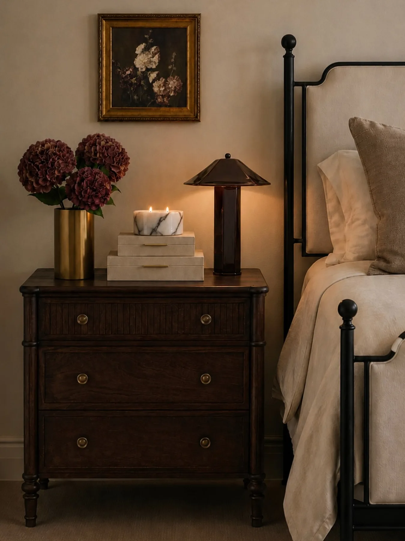 Dark wood nightstand with burgundy flowers, small black lamp, framed floral art, and cream tissue box