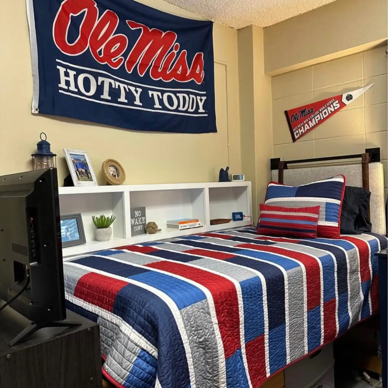 College dorm room decorated in red, navy, and white with a large Ole Miss flag and matching bedding