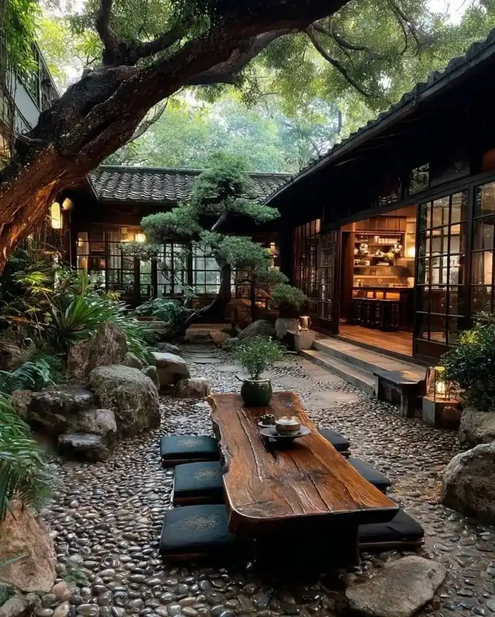 Shaded Japanese garden with a mature tree, wooden pavilion, seating area, and natural stone landscaping