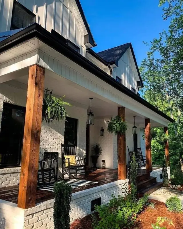 Covered porch with dark wood support posts, white siding, hanging ferns, and outdoor seating