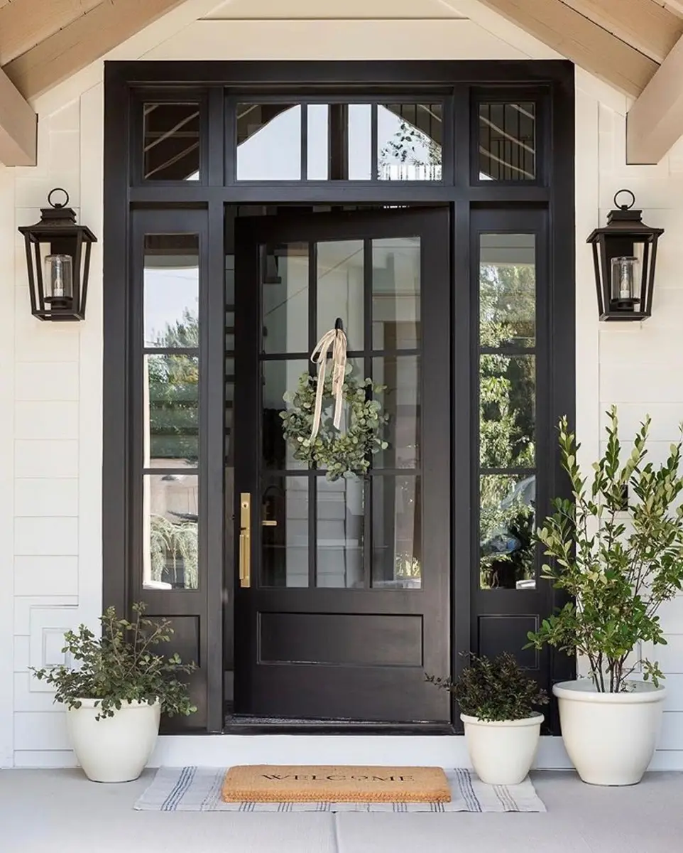 Black double front doors with glass panels, matching wall lanterns, and green potted plants