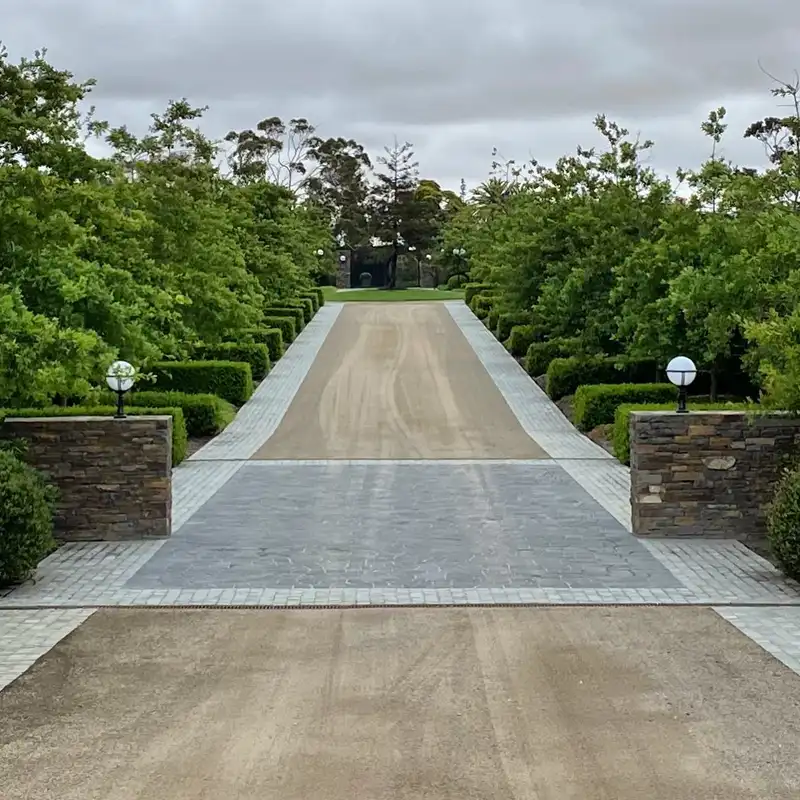 Wide paved driveway with low stone walls and simple green landscaping near the house entrance