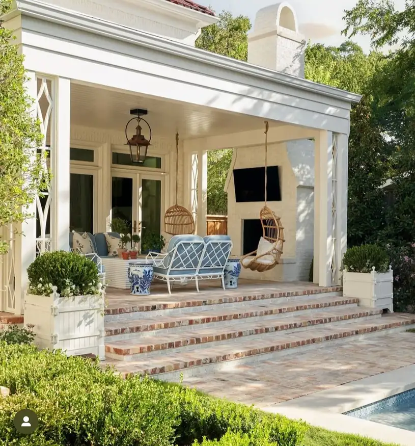 Bright covered porch with wide stone steps, white columns, wicker seating, blue cushions, and potted plants