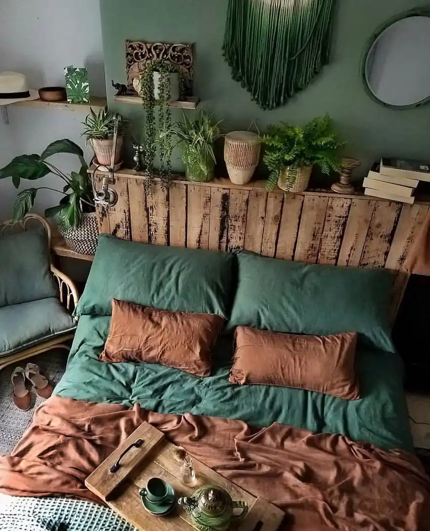 Moody green boho bedroom with forest green bedding, rust pillows, rustic wood headboard, plants, and earthy wall decor