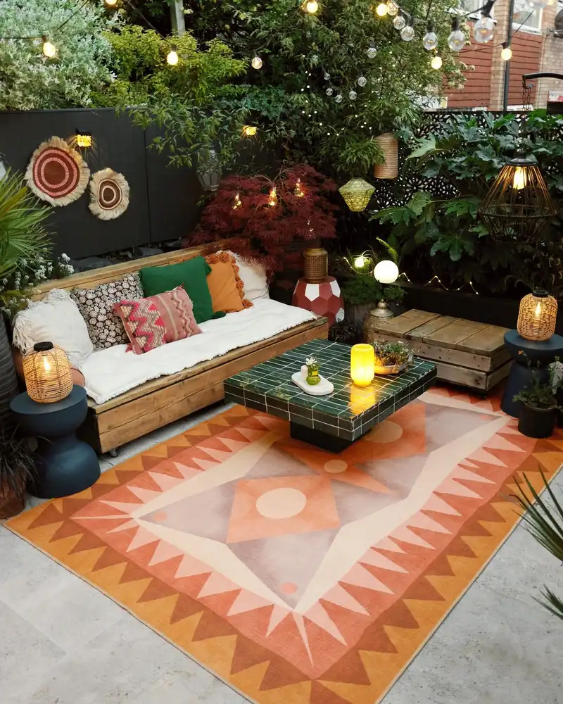 Coral geometric outdoor rug in a cozy patio with a dark green wall, warm lighting, and cushions.