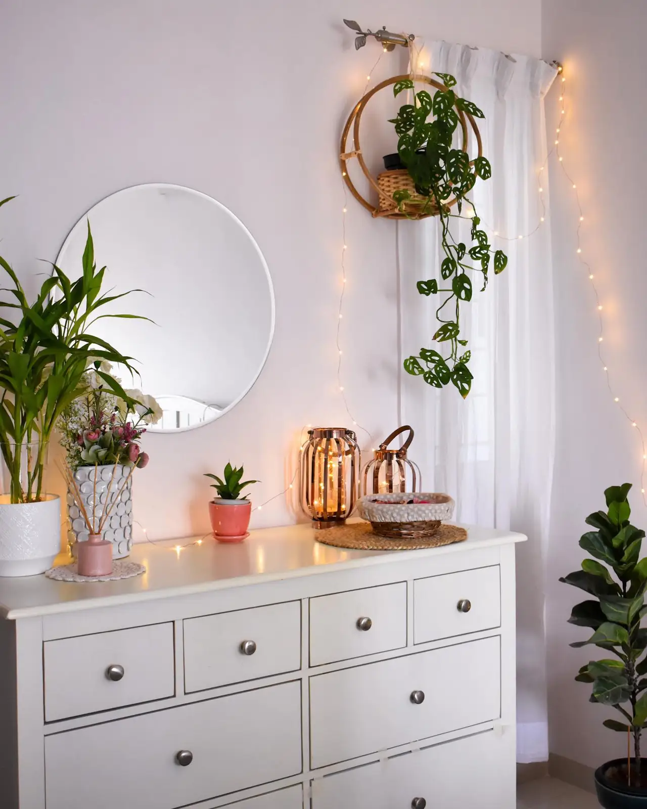 Dresser surrounded by leafy plants, hanging greenery, warm string lights, and copper-toned lanterns