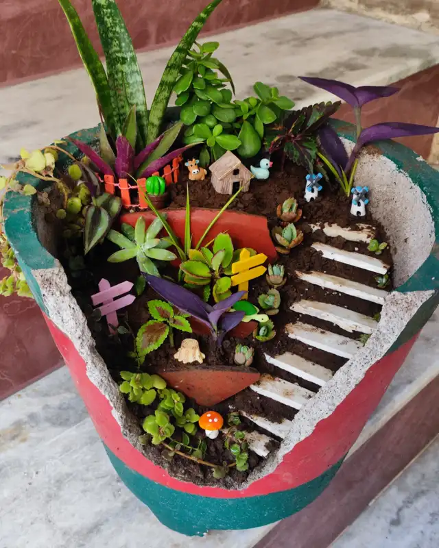 Fairy garden made from a broken terracotta pot with miniature stairs, plants, and tiny decorations