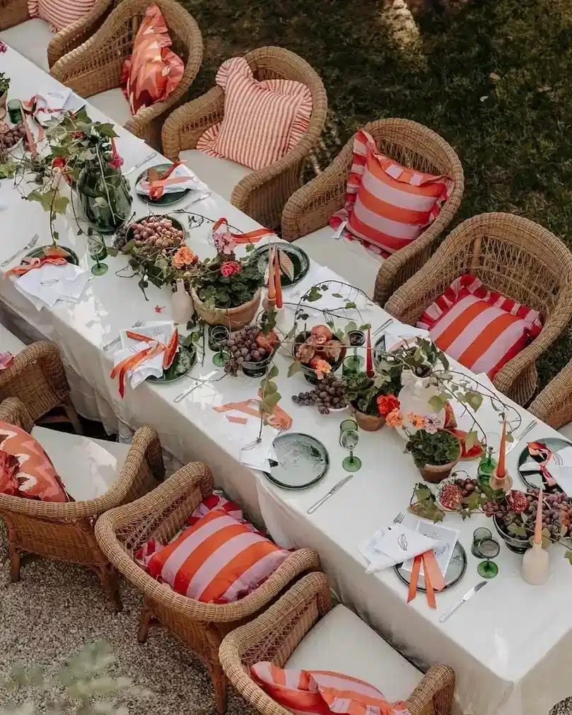 Outdoor dining table with red and white striped chair cushions, white linens, and flower arrangements