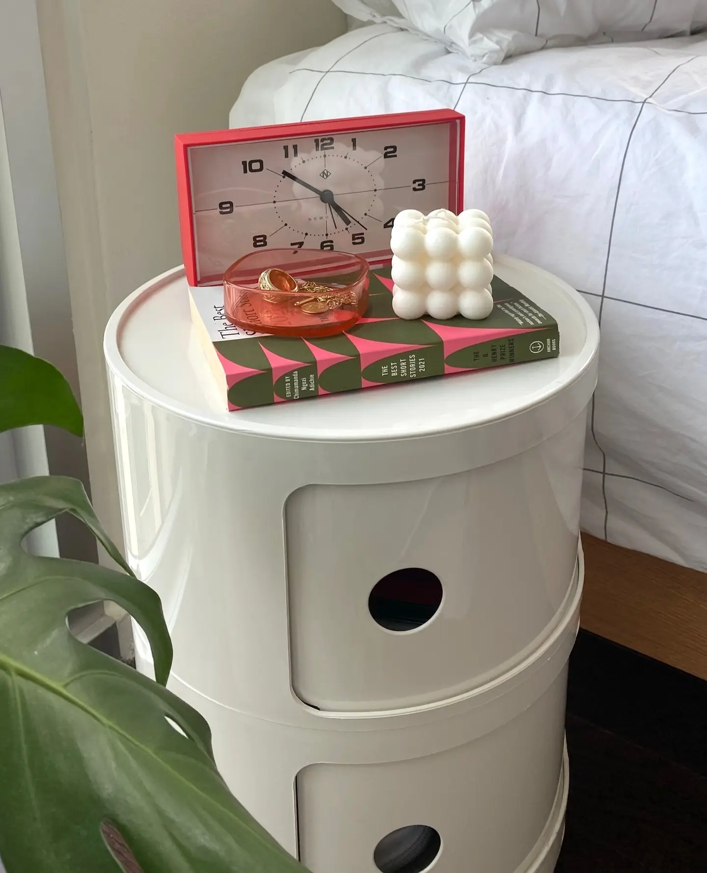 White round nightstand with red clock, bubble candle, colorful book, and small decorative dish