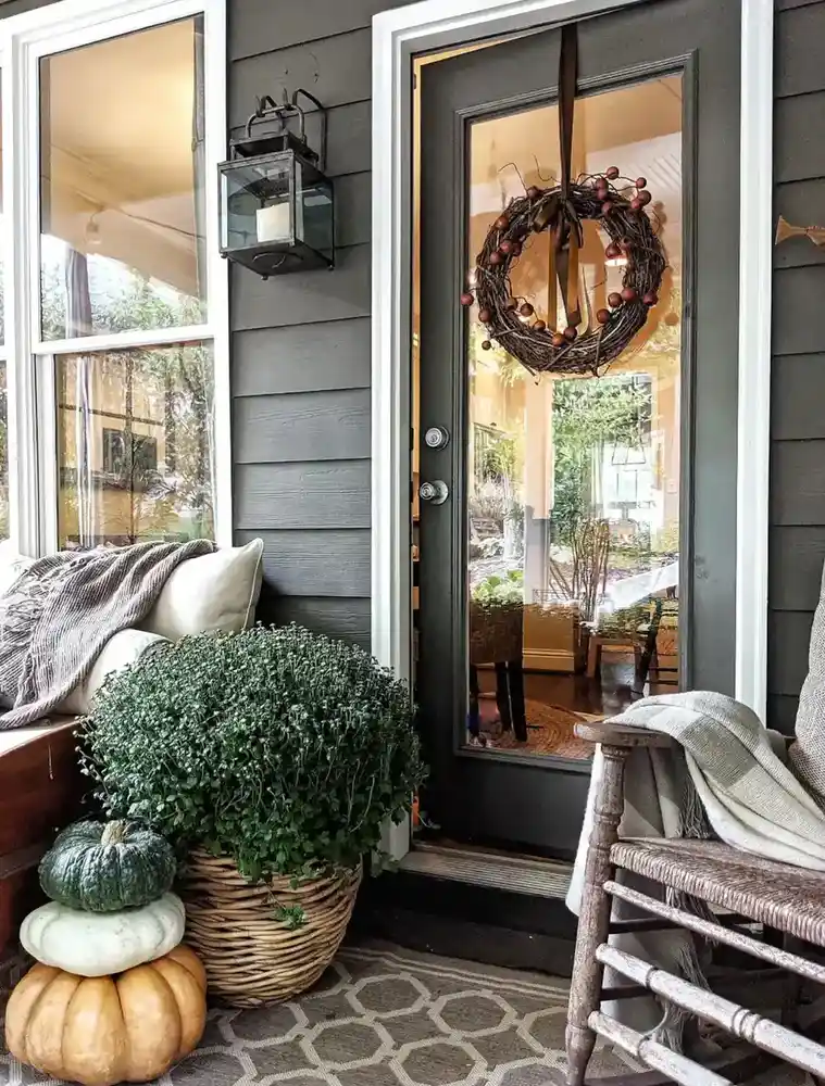 Front porch entrance with dark siding, glass door, wreath, pumpkins, greenery, and a rocking chair.