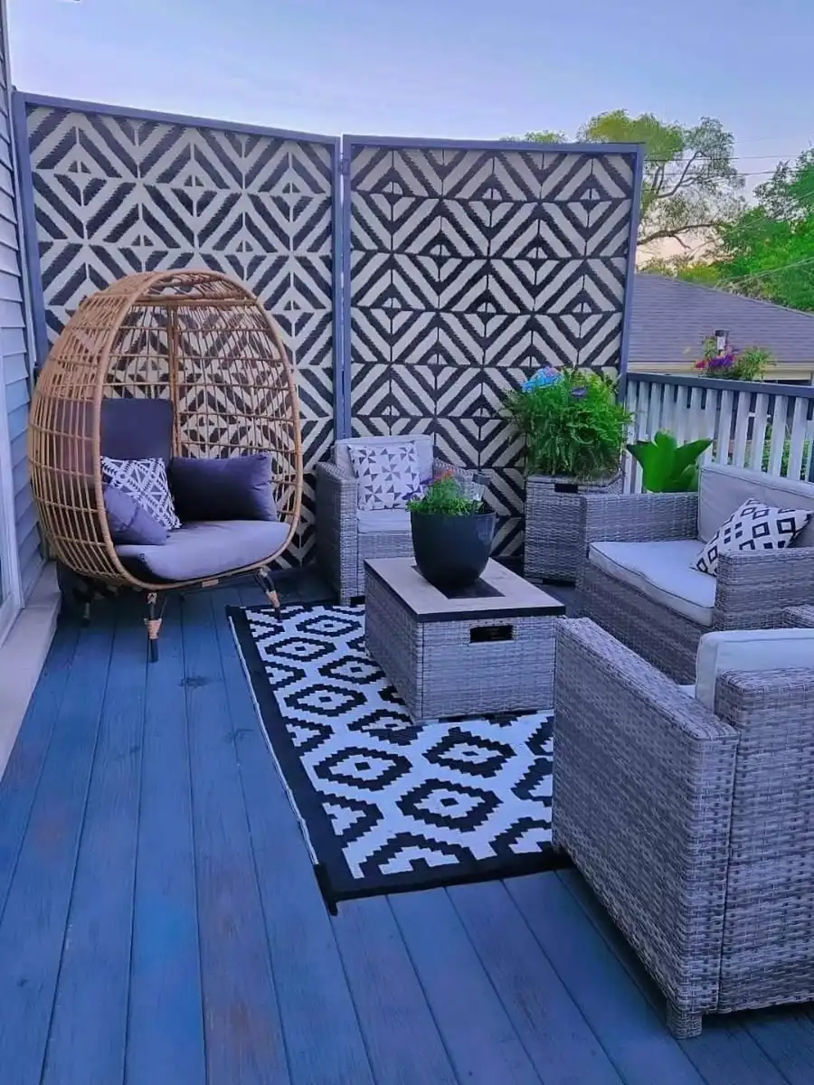 Small blue deck with gray wicker furniture, black-and-white geometric privacy screens, and hanging egg chair