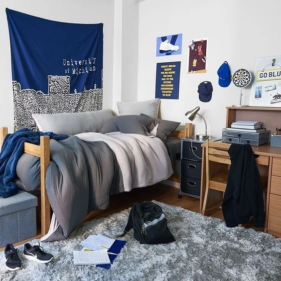 Guy's dorm room with gray bedding, a large navy wall tapestry, hats, and simple wall decor