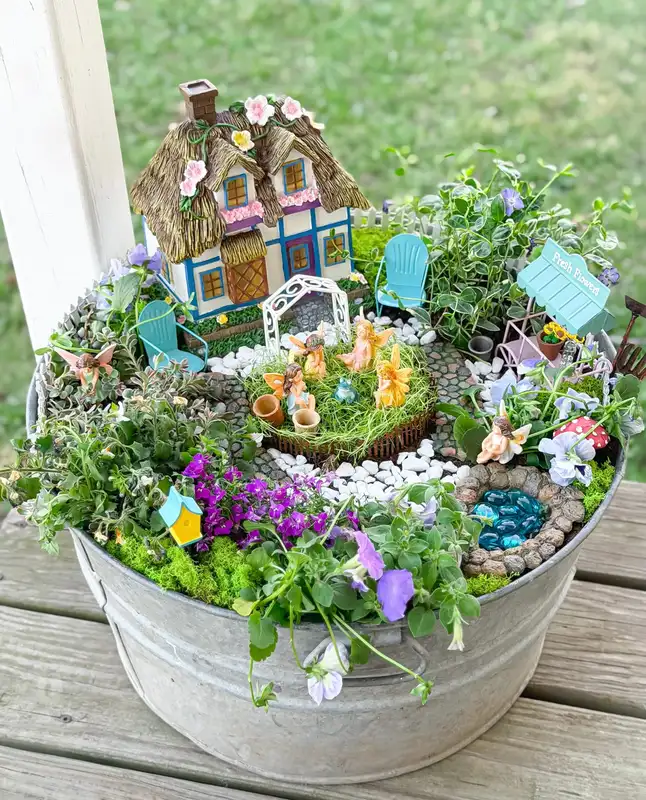 Galvanized metal tub fairy garden filled with colorful flowers, greenery, stones, and miniature houses