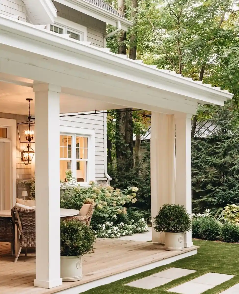 White covered porch entrance with front door, matching planters, greenery, and wide steps