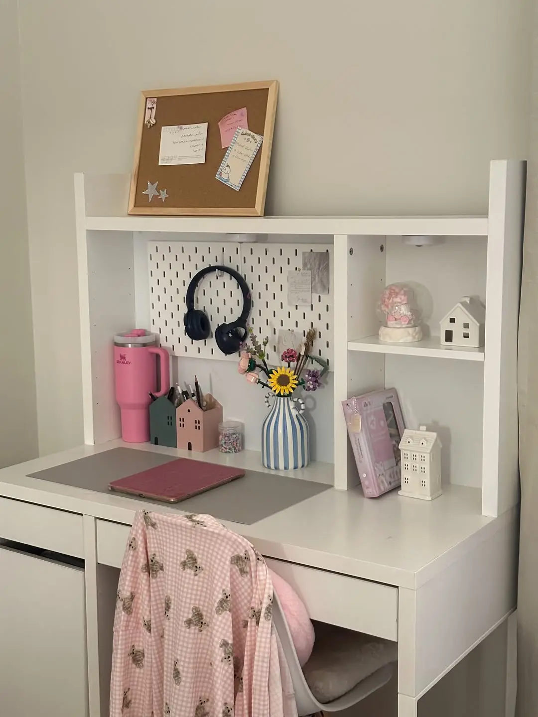 Small white dorm desk with pegboard storage, hanging headphones, shelves, and pink accents