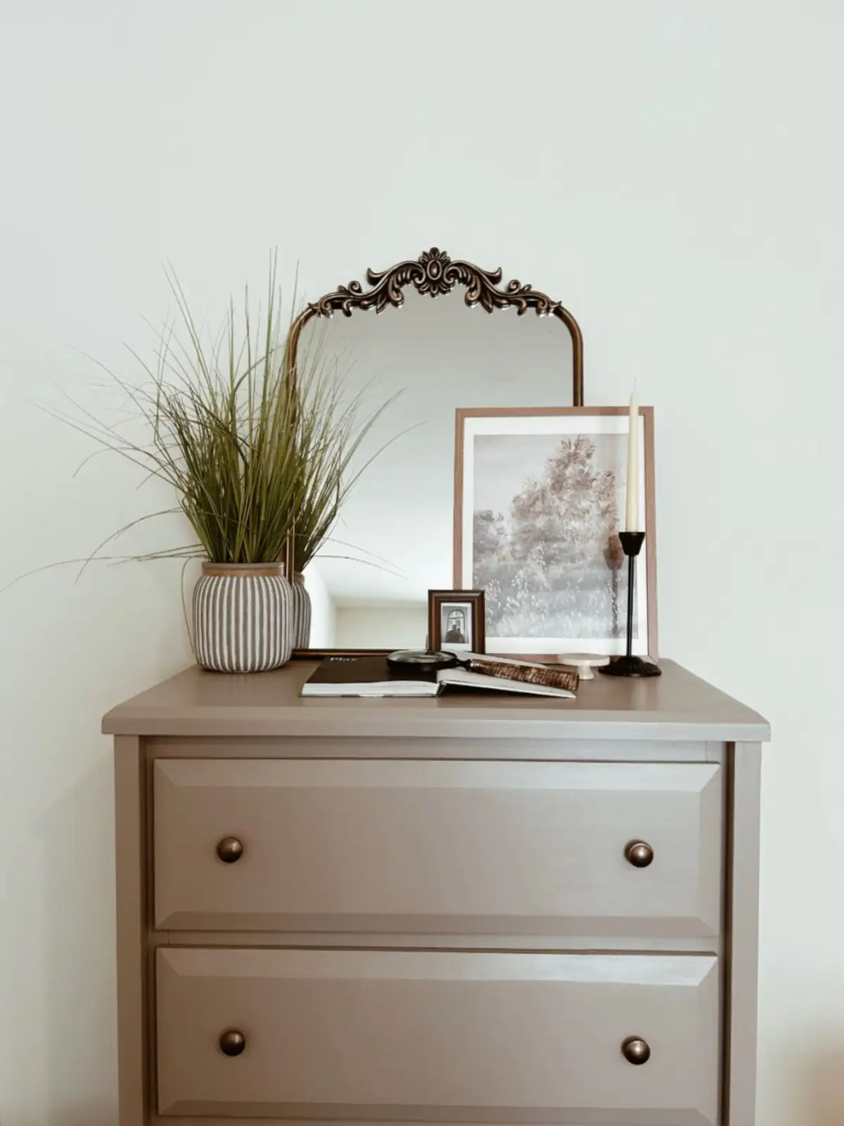 Wood dresser with leafy plant on one side and layered artwork with candlestick on the other